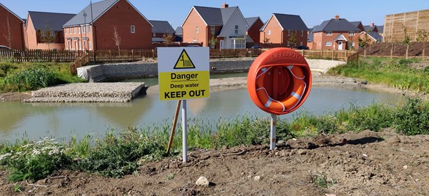 Deep pond in a housing site with 'Keep out' sign and life buoy